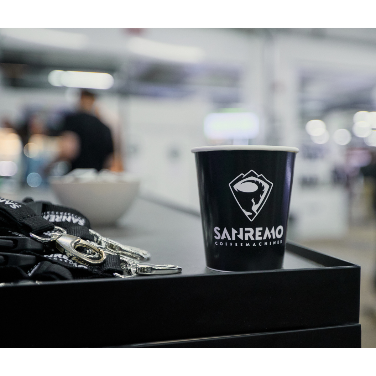 Black coffee cup with 'Sanremo' logo on a counter with keys and a blurred background - London Coffee Festival with Prime Coffee Suppliers